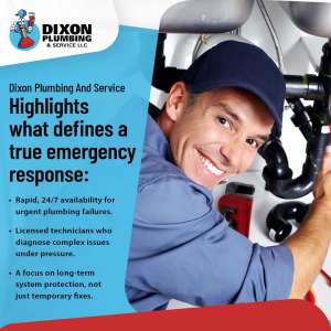 A smiling plumber in a blue uniform and cap working on pipes under a sink.
